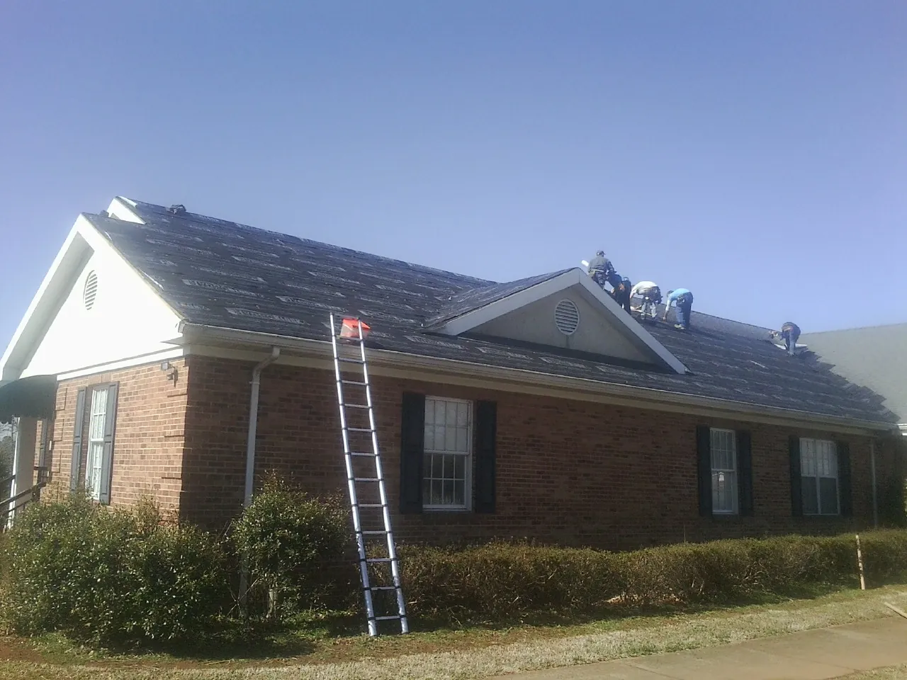 Crew tearing shingles off a brick ranch roof with a ladder set — Emergency Roof Repair work by our crew in Morgan