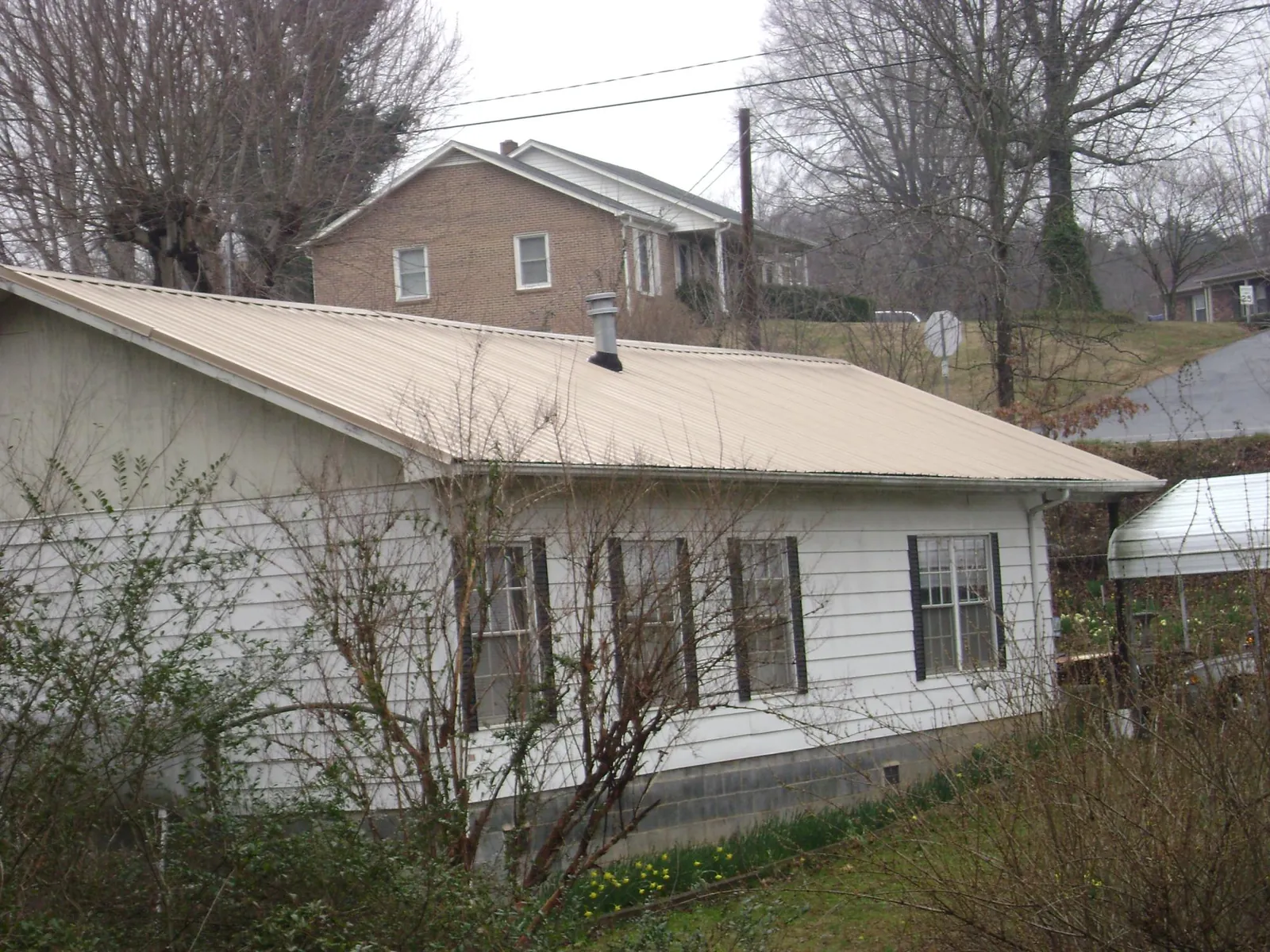 Tan metal roof on a white sided house set into a hillside — Commercial Roofing by Roofing Brothers in Morgan