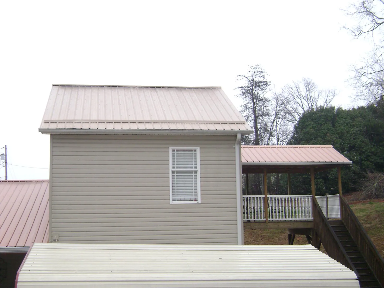 Tan metal roofs on a two story addition and attached porch, from a Roof Replacement job in Morgan